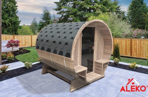Wooden barrel sauna with clear door outside in a yard.
