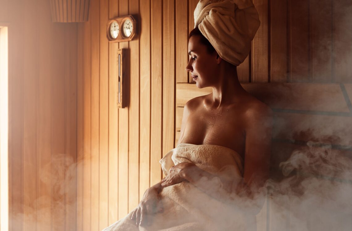 Woman wearing a towel inside a wet wooden sauna.